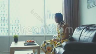 年轻漂亮的女人在家里的皮革沙发上放松，看电影微笑，喝咖啡。 3840x2160